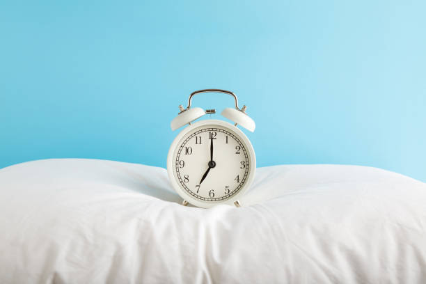 reloj despertador blanco en la almohada en el fondo de la pared azul claro. color pastel. 7 de la mañana. concepto de tiempo de vigilia. closeup. vista frontal. - clock face alarm clock clock minute hand fotografías e imágenes de stock