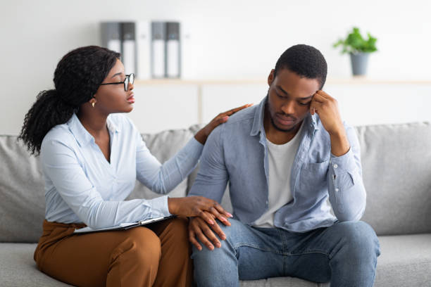 Upset black guy suffering from depression, his counselor supporting him at office Upset black guy suffering from depression, his counselor supporting him at office. Desperate male patient consulting with psychologist, receiving professional treatment of mood disorder post traumatic stress disorder photos stock pictures, royalty-free photos & images