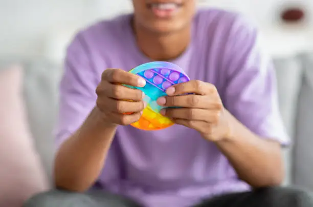 Photo of Closeup view of African American teenager playing with antistress POP IT toy at home