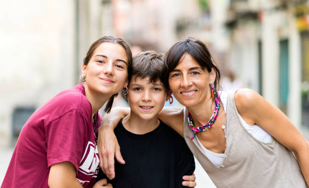portrait of three nice lovely cheerful affectionate people mom teen daughter and little son embracing outside sunny day - family child portrait little girls imagens e fotografias de stock