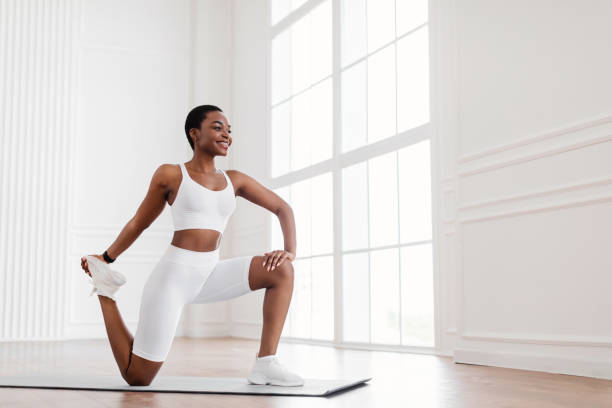 mujer negra joven estirando la pierna haciendo ejercicio en la estera de yoga - isquiotibial fotografías e imágenes de stock