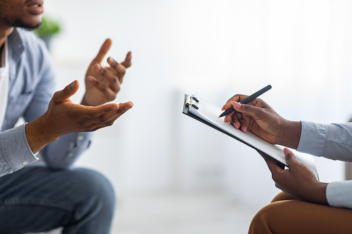 Professional psychological help concept. Unrecognizable black man talking to psychotherapist at office, closeup view. Depressed male patient having consultation with counsellor
