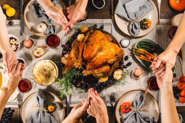 famiglia che si tiene per mano e prega durante la cena del ringraziamento - roast turkey turkey thanksgiving holiday foto e immagini stock