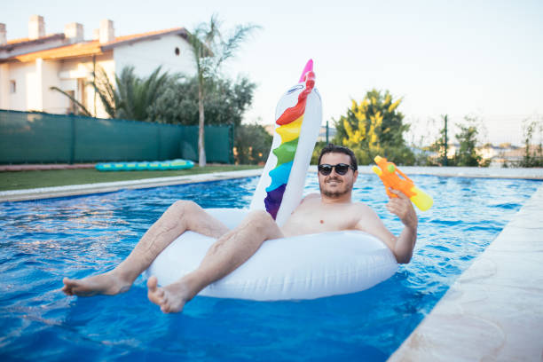 istock Man on unicorn float holding squirt gun in swimming pool 1329038110