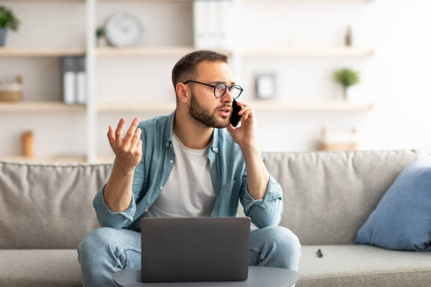 istock Stressed young freelancer using laptop and making call on smartphone at home office 1329038138