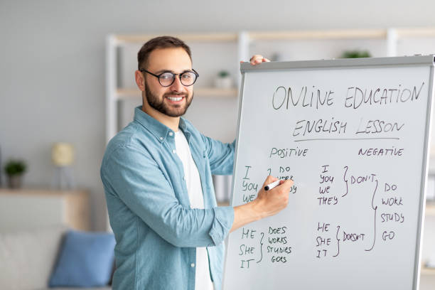 istock Positive English teacher explaining foreign language rules near blackboard indoors 1329038285