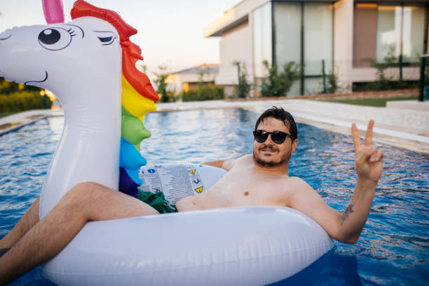 istock Man floating on inflatable unicorn in swimming pool 1329038349