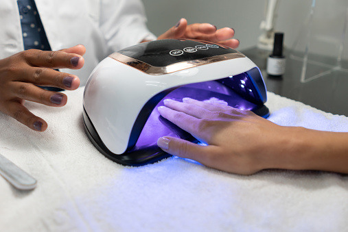 Woman getting a semi-permanent manicure with gel and drying the nail polish with a UV light lamp - beauty concepts