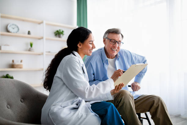 Young doctor asking senior impaired male patient in wheelchair to sign insurance policy at home Young doctor asking senior impaired male patient in wheelchair to sign insurance policy at home. Handicapped elderly man putting his signature under surgery consent form, reading medical document doctor lifestyle stock pictures, royalty-free photos & images