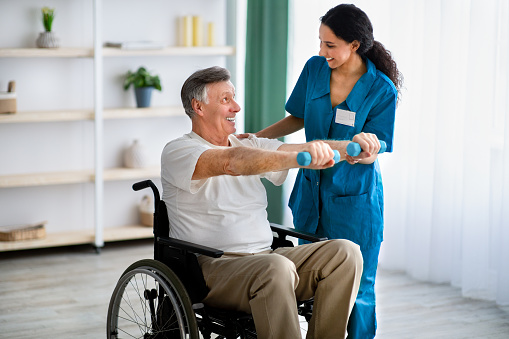 Fisioterapeuta que ayuda a un anciano en silla de ruedas a hacer ejercicios con mancuernas en el centro de salud photo