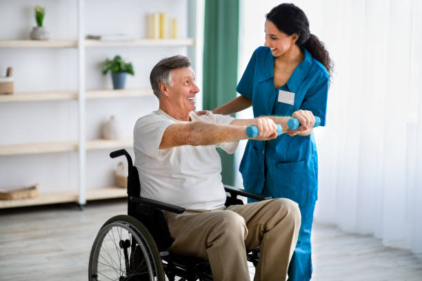 Female physiotherapist helping elderly man in wheelchair do exercises with dumbbells at health centre Female physiotherapist helping elderly man in wheelchair do exercises with dumbbells at health centre. Senior male petient undergoing rehabilitation after illness or injury at fitness clinic infarction photos stock pictures, royalty-free photos & images