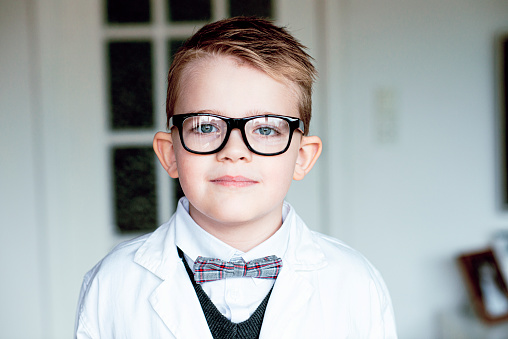 Portrait of a child scientist. He wears glasses, a bow tie  and a lab coat.  Maybe he is a child prodigy or just really interested in science.