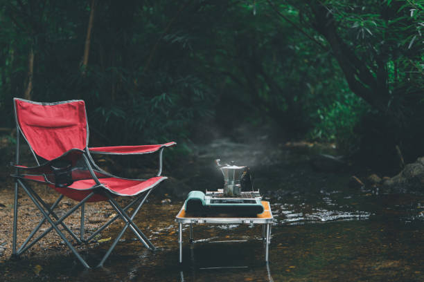 rote campingstühle stehen in einem waldbach mit kaffeezubehör. - campingstuhl stock-fotos und bilder