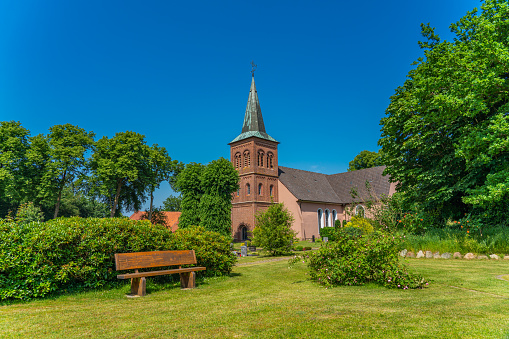 Historical Church in the village of Grossenkneten, Lower Saxony, Germany at June with green trees and blue sky in background