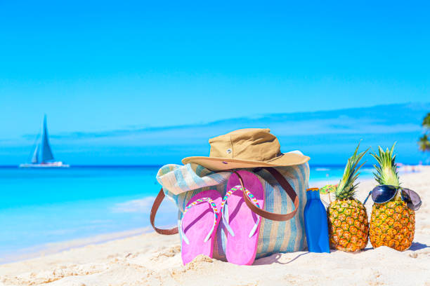 istock Beach accessories on sand for summer vacation concept. Bag, flip flops, tropical pineapples cocktails pina colada, hat and sunscreen lotion bottle on caribbean beach. Saona island, Dominican Republic. 1329050580