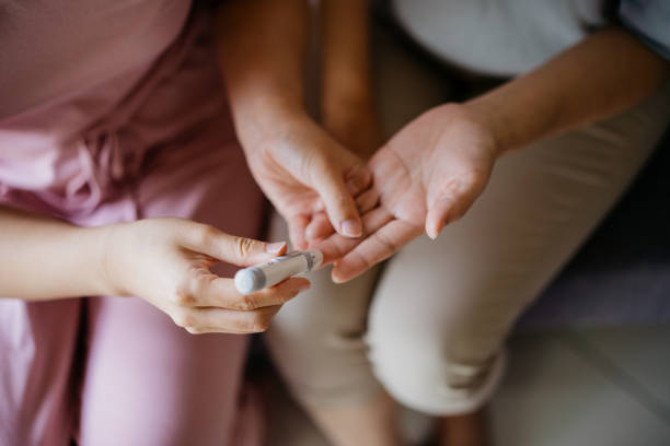 donna da vicino che aiuta sua madre a controllare il livello di zucchero nel sangue a casa - hypoglycemia foto e immagini stock