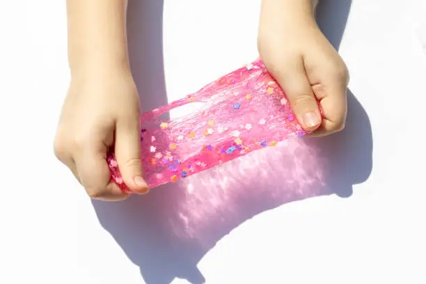 Photo of hands of a little girl with pinky shiny transparent slime close up on white background