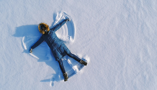 Woman makes snow angel laying in the snow. Top view