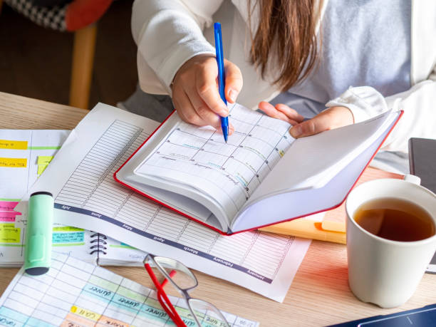 woman writing schedule In calendar notebook on a desk Close-up Of A woman writing schedule In calendar notebook on a desk with paperwork and coffee cup. Planning, time management and organizing. Woman hand writing on an agenda. time management student stock pictures, royalty-free photos & images