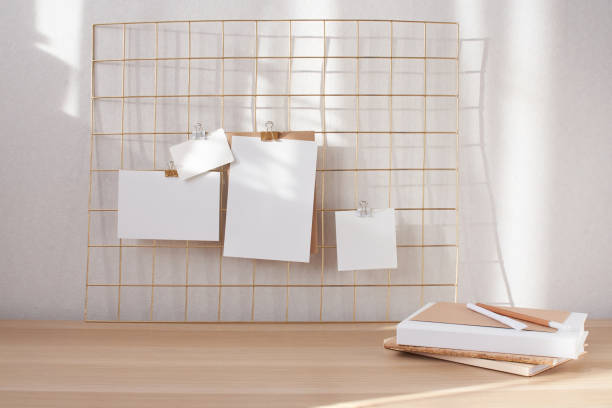 istock Blank white cards, poster mock up attached on gold grid board. Stack of notebooks on desk. 1329061641