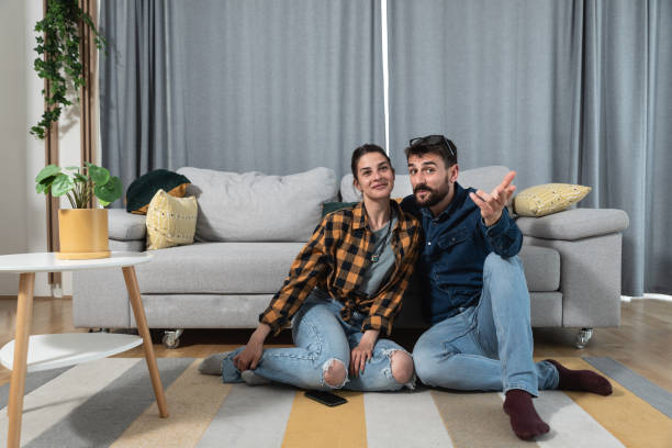 pareja joven sentada en el suelo viendo el partido deportivo en la televisión y el hombre explicando a la mujer las reglas en el juego porque ella no es una persona de tipo deportivo y no conoce las reglas - tennis couple women men fotografías e imágenes de stock