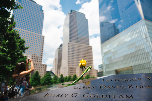 New York City, USA - July 6, 2016: A yellow rose is left at the National September 11 Memorial at Ground Zero in Lower Manhattan. Rising behind it is One World Trade Center (also known as the Freedom Tower), built after the 9/11 attacks.