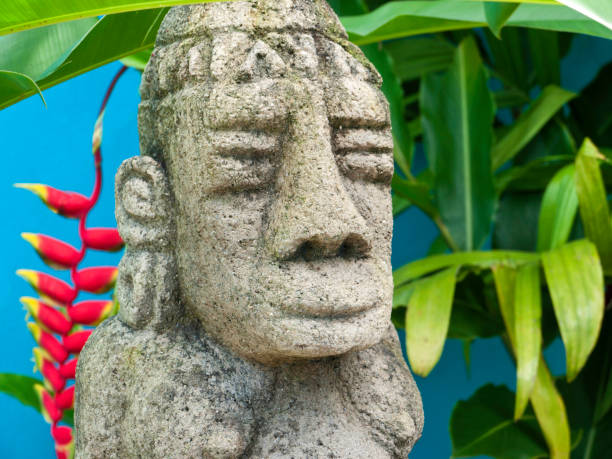 Costa Rican Sculpture of Mayan diety in outdoor setting with banana leaves and heliconia plant in background stock photo