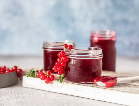 Homemade red currant jam or jelly in glass jars and red currants fresh berries on wooden cutting board. Selective focus.