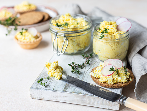 Tartlets with egg pate or salad and radish and thyme on light stone background. Egg dip in glass jar. Selective focus.