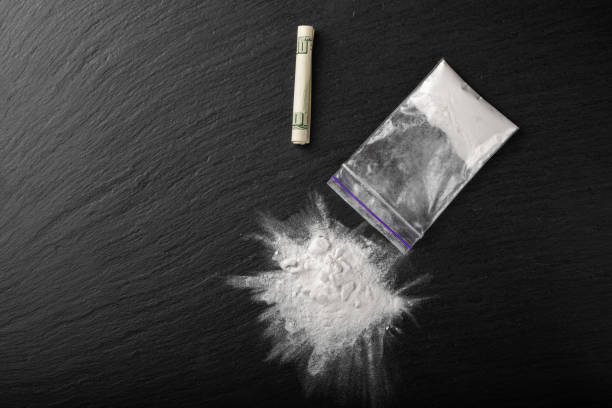 istock Cocaine in a plastic package on a black background, close-up. A rolled up dollar bill for drug use. 1329068267