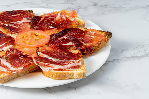Plate of toast with delicious Iberian ham with a slice of tomato. Typical Spanish dish. Copy space.
