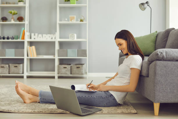 istock Smiling young student looking at laptop screen and taking notes during online lesson 1329080157