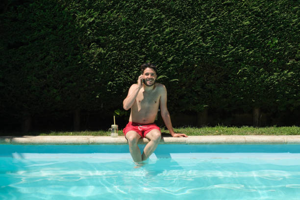 istock Young man talking on his smartphone sitting on the swimming pool edge. Summer concept. 1329081486