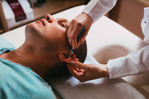 Man lying down and having an acupuncture treatment on his ear in an alternative medical clinic