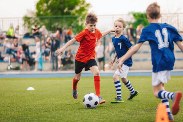 group of boys in two kids soccer teams competing for the ball on a football tournament match. soccer school children playing game on grass pitch. football stadium full of fans in background - soccer ball youth soccer event soccer imagens e fotografias de stock