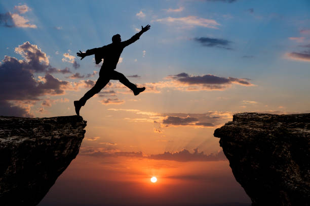istock Silhouette of man jumping from one cliff to another cliff 1329092994