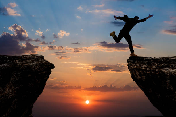 istock Silhouette of man jumping from one cliff to another cliff 1329092995