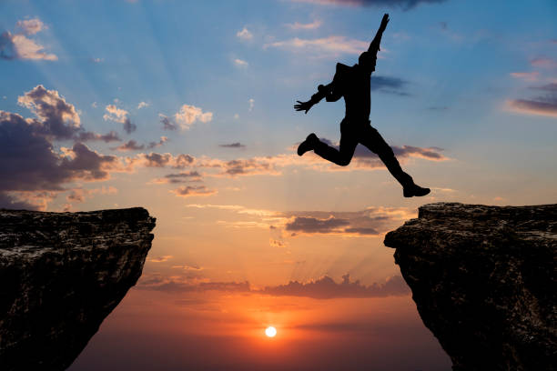 istock Silhouette of man jumping from one cliff to another cliff 1329092997