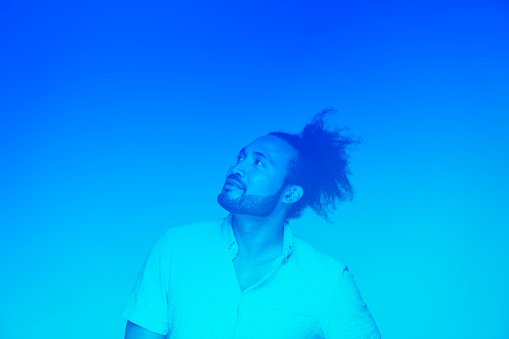 Black man with frizzy hair in knot looking upward int blue against blue hue and background