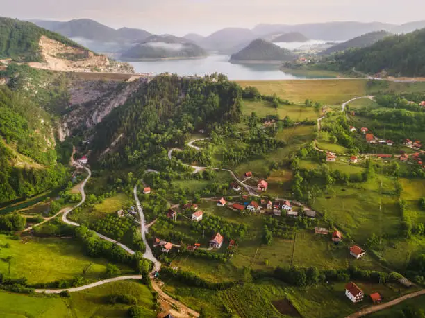 Photo of Tranquil view of remote mountain village with lake in misty summer morning. Nature outdoors travel destination, National park Tara, Zaovine lake, Serbia