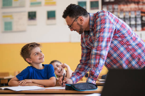 istock Kid looking at his teacher standing by a desk and smiling 1329102072