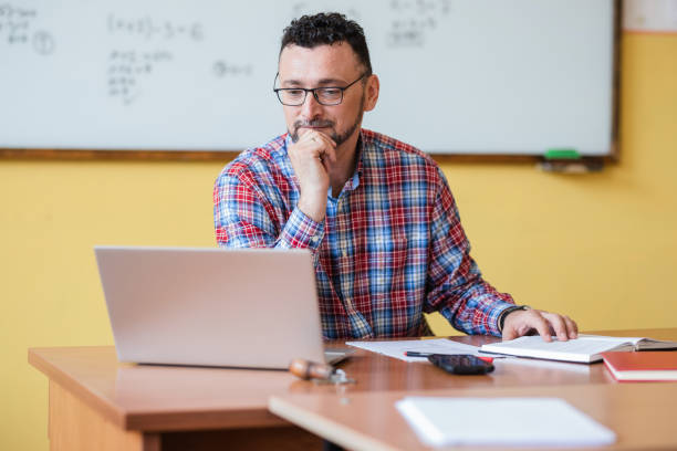 Teacher working on laptop Man sitting at classroom and using laptop instructor stock pictures, royalty-free photos & images