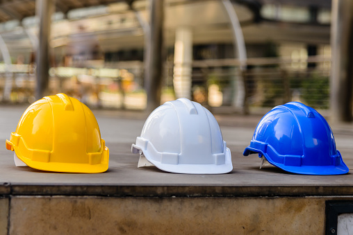 Yellow, white and blue hard safety helmet hat for safety project of foreman, engineer and worker on the concrete floor. Protective head hardhat of worker lined up on construction site floor in city.