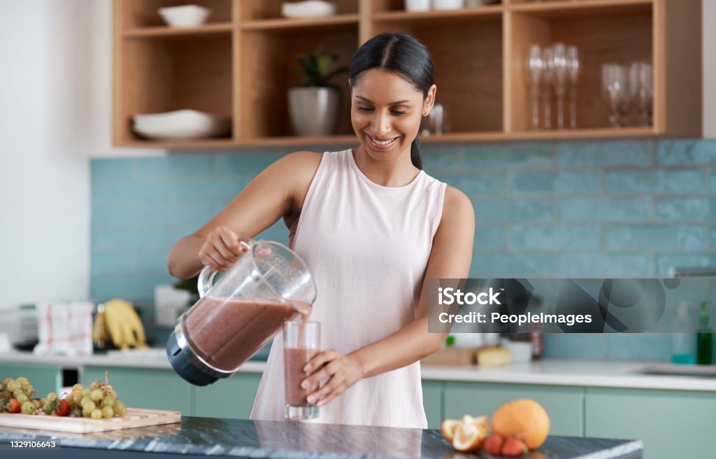 Cropped shot of an attractive young woman making smoothies in her kitchen at home A smoothie cures all Smoothie Stock Photo