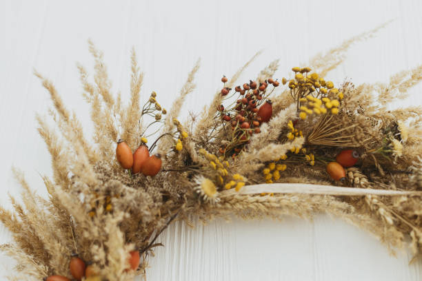 istock Stylish autumn rustic wreath close up. Creative boho wreath with dried pampas grass, tansy wildflowers, wheat, dog-rose berries on white wooden table. Fall decor details 1329107617