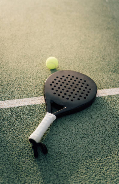 raqueta de pádel y pelota de pádel en una pista verde al atardecer - racketball racket ball court fotografías e imágenes de stock