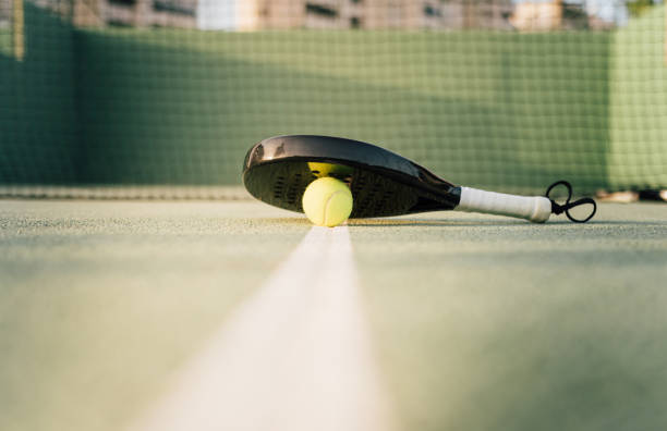 raqueta de pádel y pelota de pádel en una pista verde al atardecer - racketball racket ball court fotografías e imágenes de stock