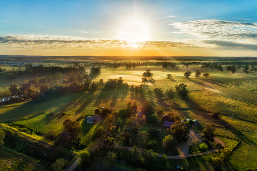 Secluded farm homestead on agriculture cultivated fields near Macquarie river in Dubbo town of Australia - aerial sunrise view.