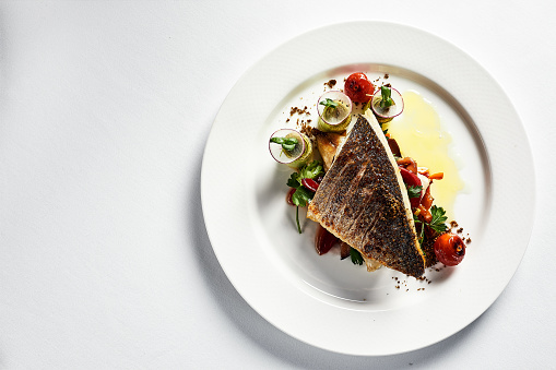 Grilled seabass with vegetables top view, close-up, white plate, light background, copy space.