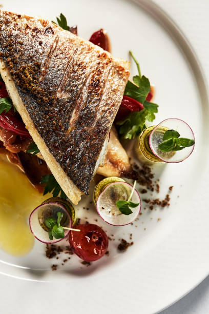 istock Grilled seabass with vegetables with a brown crust top view, close-up, white plate 1329114834